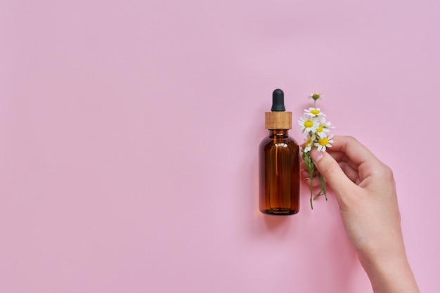 Main de femme fleurs et bouteille en verre avec produit cosmétique sur fond rose