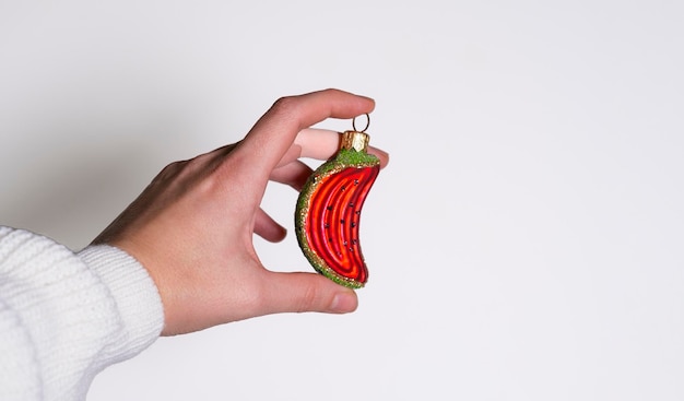 la main d'une femme sur fond blanc tient un jouet de Noël en verre sous la forme d'une pastèque