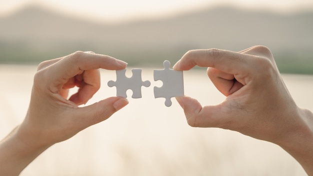 Main de femme et d'homme reliant un morceau de puzzle sur fond de montagne et de lac