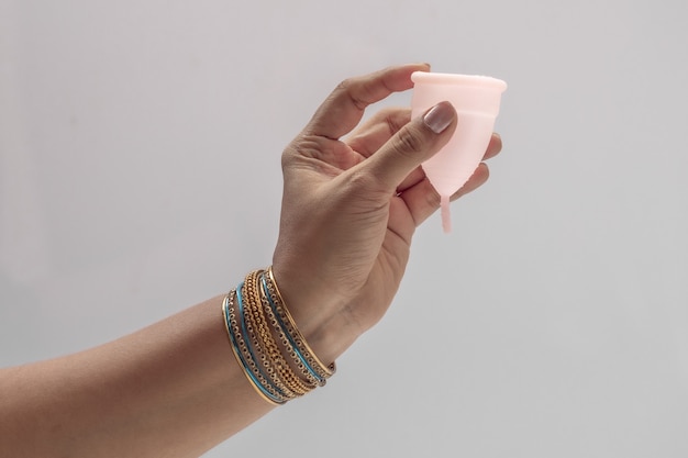 Une main de femme indienne tenant une coupe menstruelle en silicone réutilisable et montrant différents types de pliage.