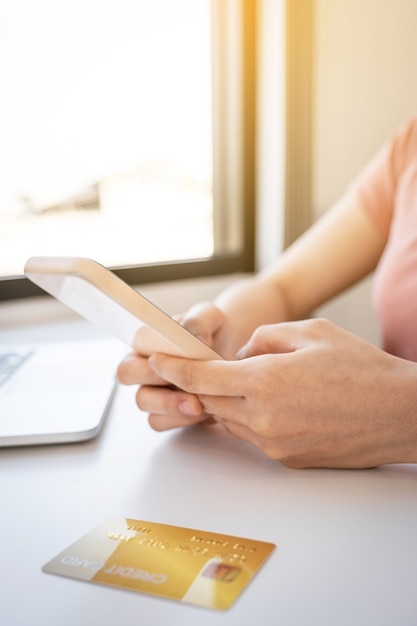 Main de femme jeune consommateur asiatique à l'aide de smartphone et ordinateur portable pour magasiner en ligne