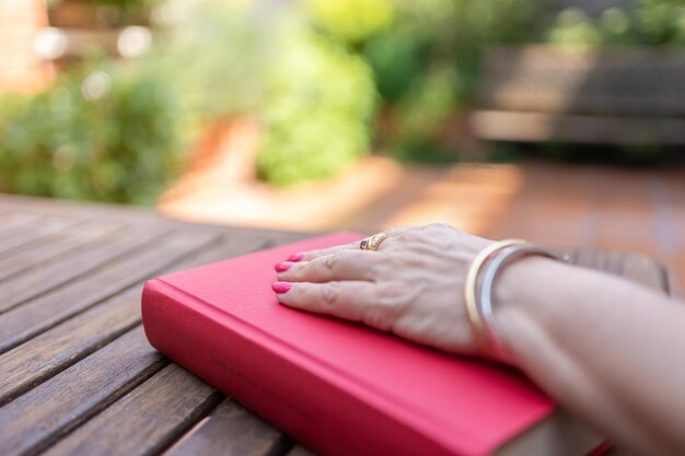 Main de femme sur un livre fermé sur une table de jardin avec des aperçus du soleil