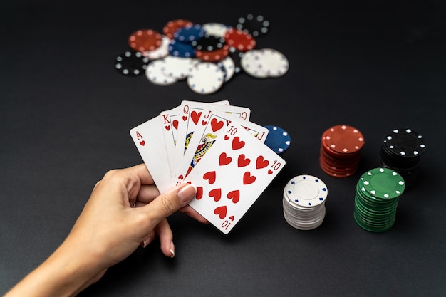 Main de femme avec la main de la quinte royale jouer aux cartes avec des jetons de poker. Concept de jeu de poker