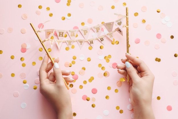 La main de femme avec une manucure pastel tient une petite bannière joyeux anniversaire. Salutations de joyeux anniversaire sur fond rose avec des confettis