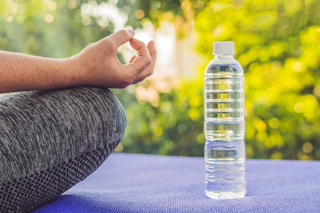 Main d'une femme méditant dans une pose de yoga sur un tapis et une bouteille d'eau