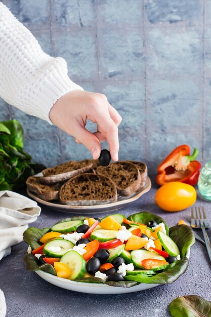 La main d'une femme met une olive dans une salade grecque fraîchement préparée sur une assiette Vue verticale