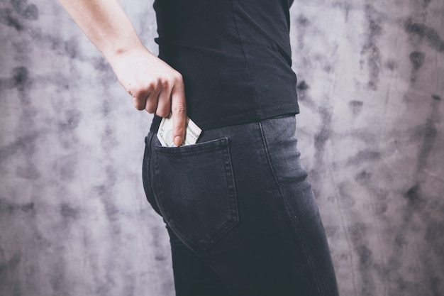 Main de femme mettant de l'argent dans la poche de jeans