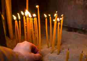 Photo main de femme a mis une bougie de cire sur la flamme pour prier à l'église. des bougies en cire d'abeille brûlent dans le temple