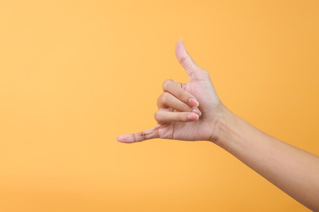 La main de la femme montrant un geste de la main d'appel ou un signe de shakah sur fond jaune