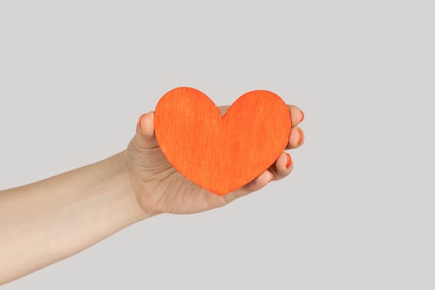 Main de femme montrant un petit coeur en papier rouge, symbole d'amour et de dévotion