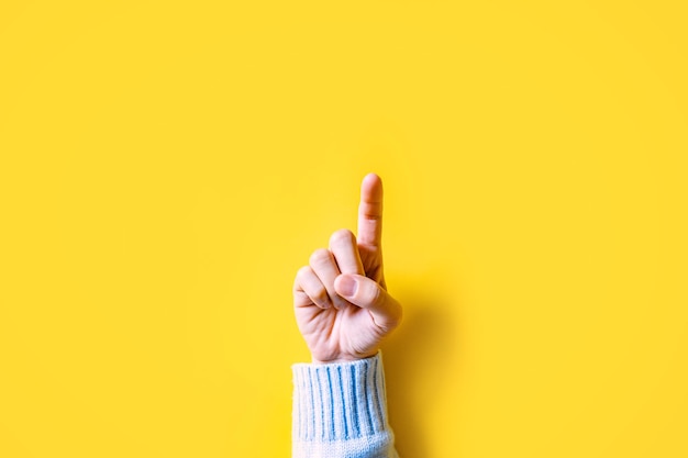 Photo la main de la femme montre l'index vers le haut pointant vers le haut sur fond jaune