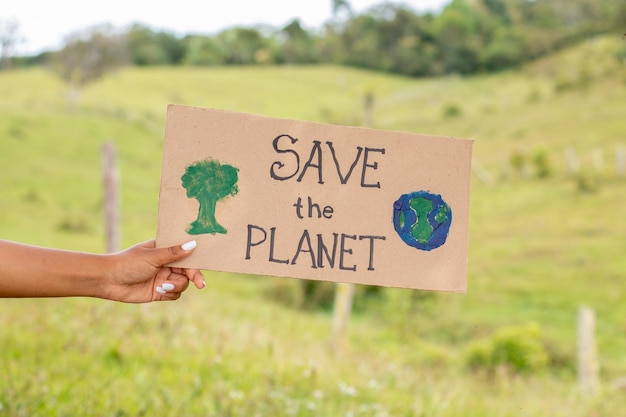 Main de femme noire tenant une pancarte demandant de sauver la planète sur un fond de nature verdoyante