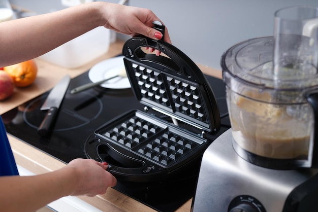 Main de femme ouvrant le couvercle du multibaker pour faire des gaufres viennoises près du gros plan du robot culinaire