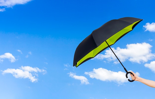 Main de femme avec un parapluie sur fond de ciel bleu.