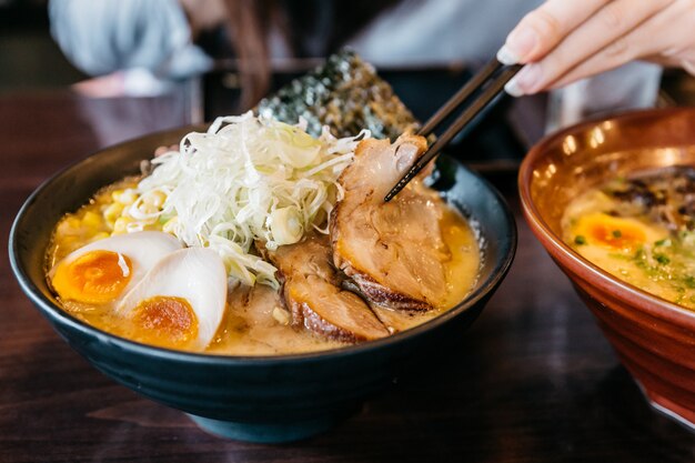 Main de femme pince-nouilles dans la soupe aux os de porc Ramen (Tonkotsu Ramen).