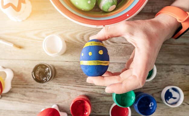 La main d'une femme avec un pinceau dessine un motif coloré sur un œuf de Pâques Préparation créative pour des vacances de Pâques lumineuses