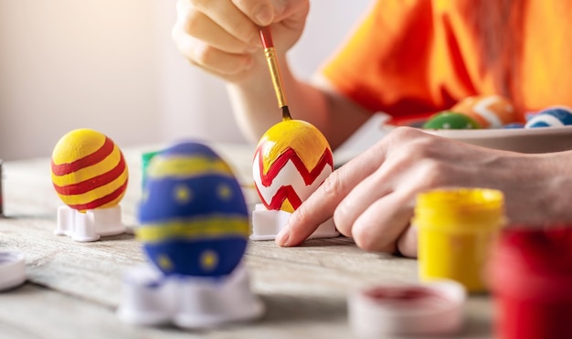 La main de la femme avec un pinceau dessine un motif coloré sur un oeuf de Pâques Préparation pour les vacances de Pâques lumineuses