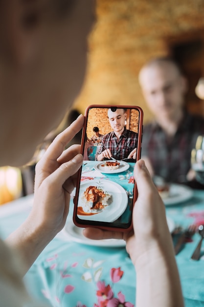 La main d'une femme prenant un portrait de son assiette de nourriture et de son partenaire.