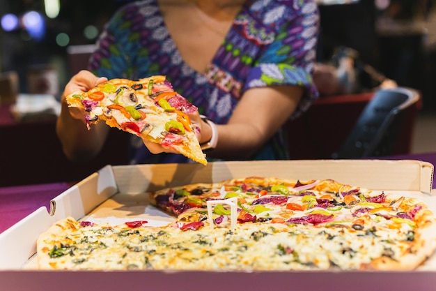 Main de femme prenant une tranche de pizza new-yorkaise dans une boîte à emporter