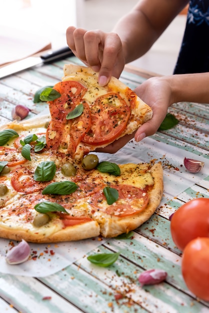 Main d'une femme prenant une tranche de pizza vue de dessus sur des planches turquoises rustiques