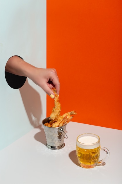 La main d'une femme prend des crevettes frites dans un seau en métal à travers un trou de papier de la bière d'ombre dure moderne de haute qualité...