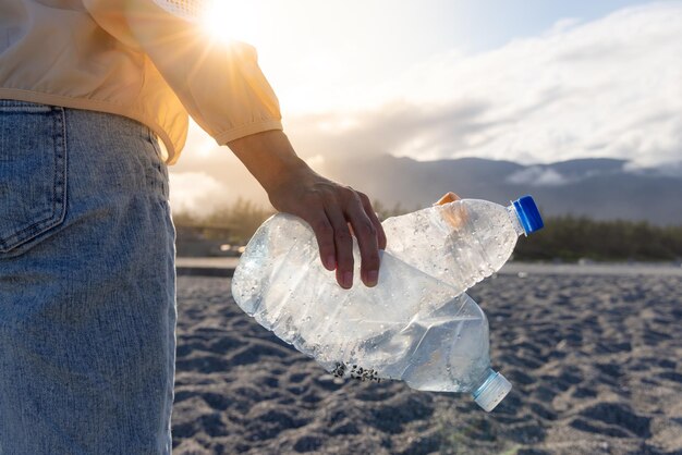 La main de la femme ramassant une bouteille en plastique nettoyant sur la plage