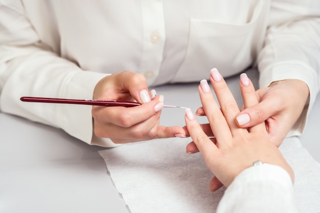 La main de femme reçoit une manucure par une esthéticienne des ongles se bouchent.