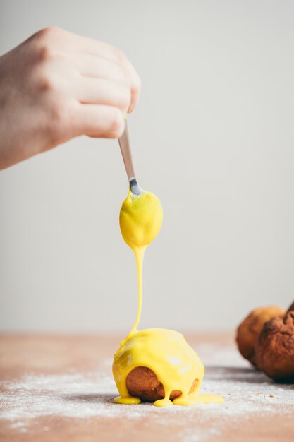 Main de femme recouvrant un beignet de glaçage jaune.