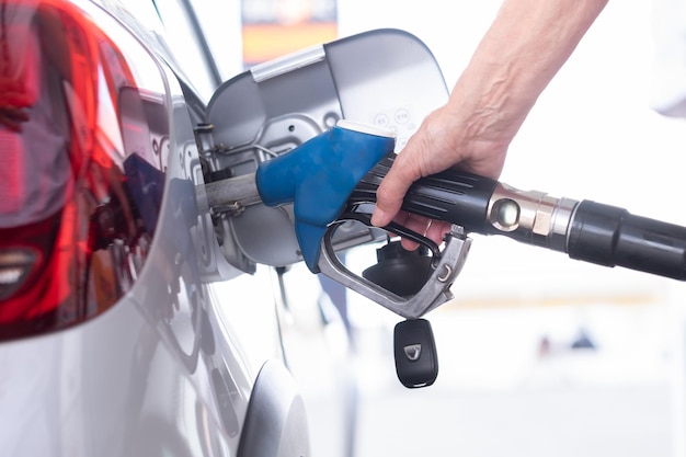 Main de femme remplissant le carburant dans le réservoir de la voiture à la station-service de la pompe pour l'augmentation des prix de l'inflation