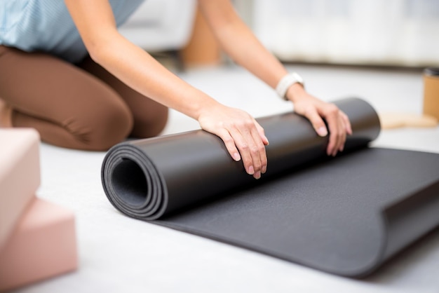 La main de la femme roule le tapis de yoga à la maison