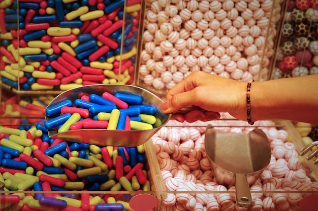 Main de femme avec scoop prenant de délicieux bonbons colorés sur le comptoir du café du marché de l'épicerie