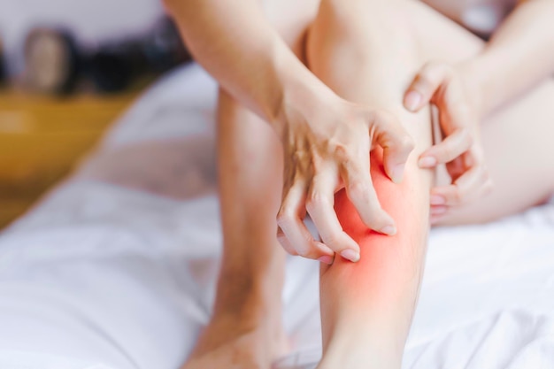 Photo main de femme se grattant la jambe au lit en raison d'une réaction allergique