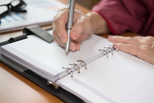 Main de femme avec un stylo écrivant une note sur un ordinateur portable au bureau