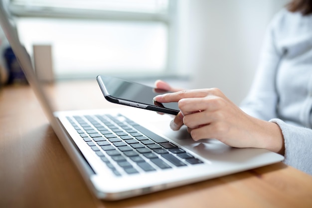 Main de femme tapant sur un clavier d'ordinateur portable avec un téléphone portable