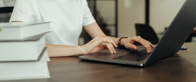 Main de femme tenant appuyez sur le bouton sur l'ordinateur portable du clavier et la pile de livres.