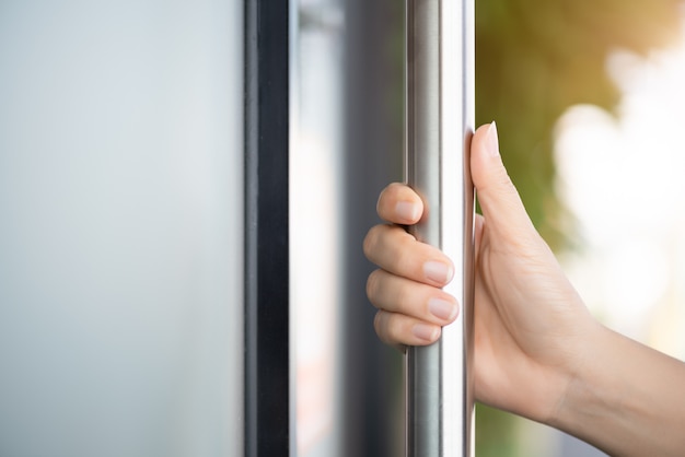 Main de femme tenant la barre de porte pour ouvrir la porte avec fond de réflexion en verre.