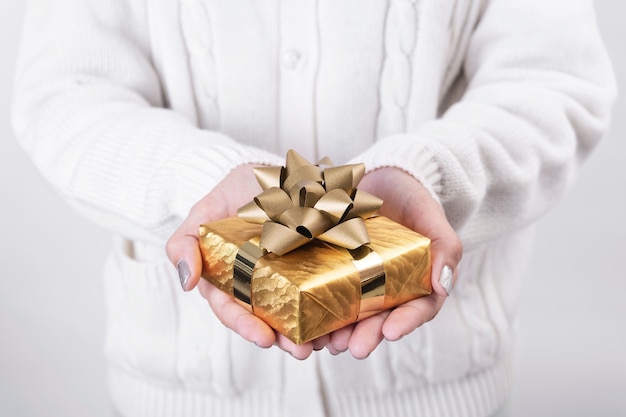 Main de femme tenant la boîte-cadeau or sur fond blanc.