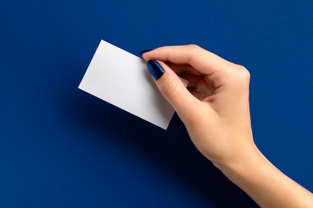 Main de femme tenant une carte papier sur fond bleu. Salon de beauté maquette modèle de carte de voeux