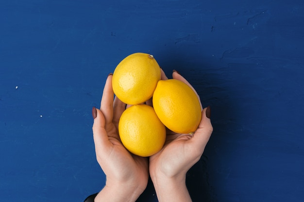 Main de femme tenant le citron contre le bleu classique