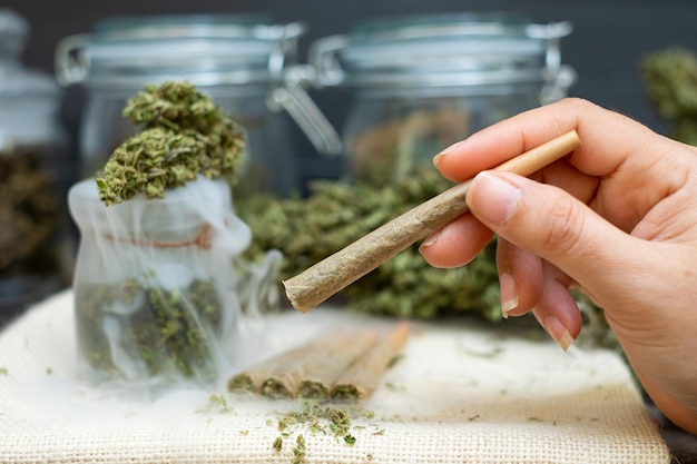 Main de femme tenant des cônes préroulés pour fumer du cannabis avec du cannabis indica dans une bouteille transparente