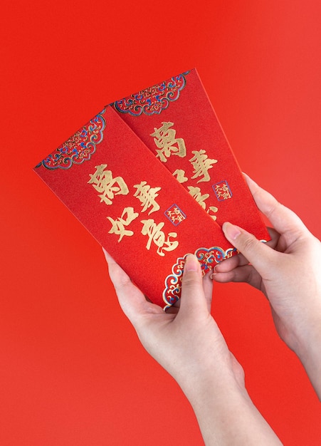 Main de femme tenant une enveloppe rouge ou un paquet rouge cadeau monétaire ou Ang pao avec une phrase chinoise signifie tout ou tout ce qui compte Concept du Nouvel An chinois Rouge isolé