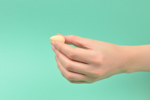 Main de femme tenant une éponge de beauté sur fond vert.