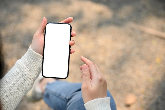 La main d'une femme tenant une maquette d'écran blanc de smartphone sur une rue floue en arrière-plan