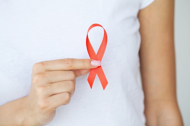 Main de femme tenant le ruban rouge VIH, ruban de sensibilisation de la journée mondiale du sida.