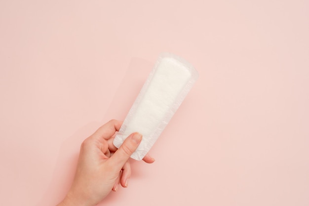 Main de femme tenant une serviette hygiénique sur fond rose