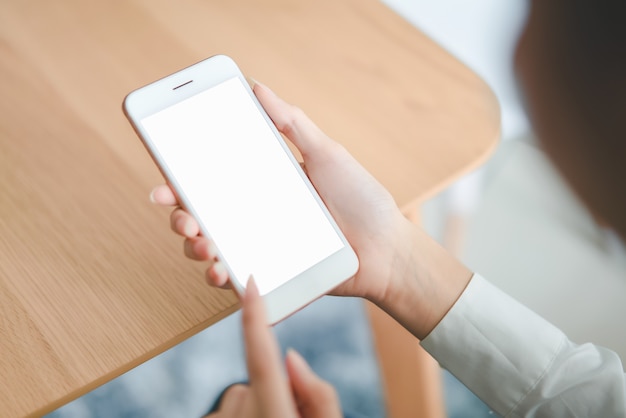 Main de femme tenant le smartphone avec un écran blanc sur la table à café.