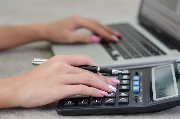 Main de femme tenant un stylo et une calculatrice. Finance, fiscalité et investissement.