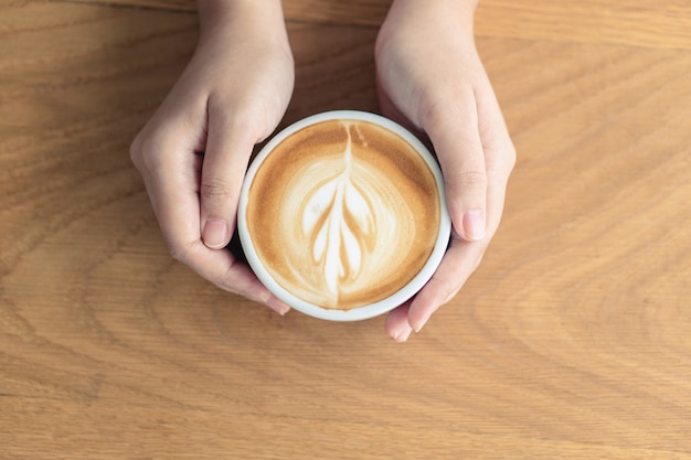 Main de femme tenant une tasse de café blanche. Le café est un café au lait. table sur le bois