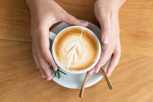 Main de femme tenant une tasse de café blanche. Le café est un café au lait. table sur la table en bois