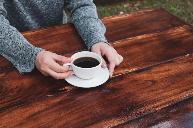 Main de femme tenant une tasse de café sur une table en bois